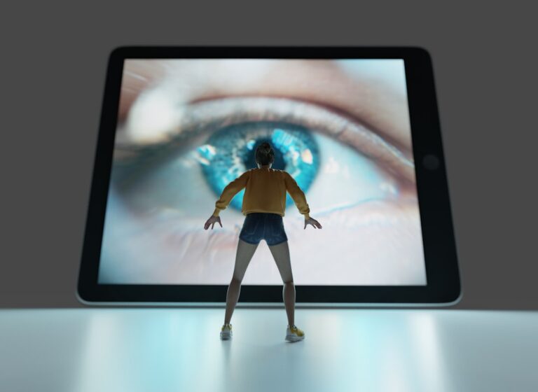 A person sitting at a home office desk, looking away from a computer screen and stretching their eyes.