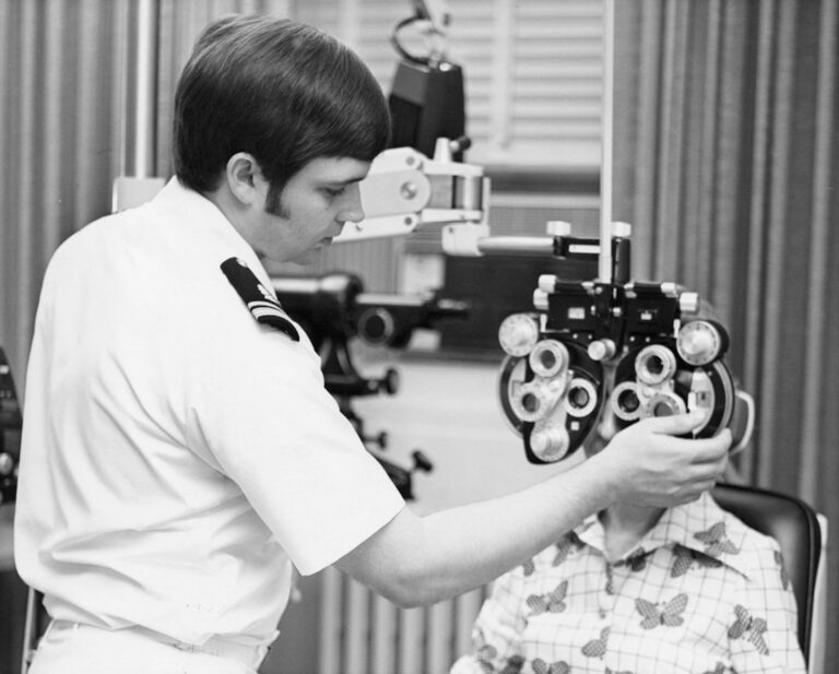 A young child sitting in an exam chair, looking at a vision chart with an optometrist pointing.